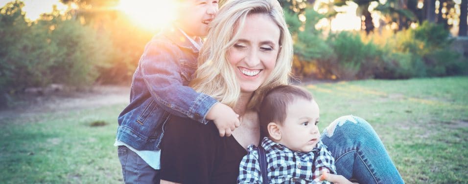 woman holding baby sitting on green grass field under sunset