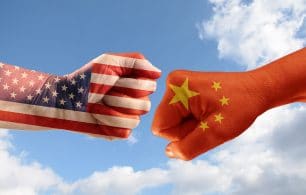 Trade conflict, fists with the flags of USA and China against each other, blue sky with clouds in the background