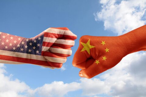 Trade conflict, fists with the flags of USA and China against each other, blue sky with clouds in the background