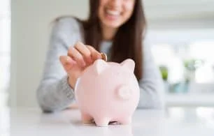 Young woman smiling putting a coin inside piggy bank as savings for investment