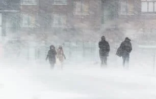People looking cold, hurrying through a blizzard in winter, against drab buildings