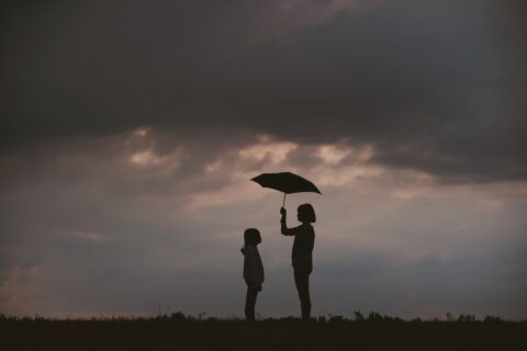 woman and child under an umbrella against a grey cloudy background in black and white