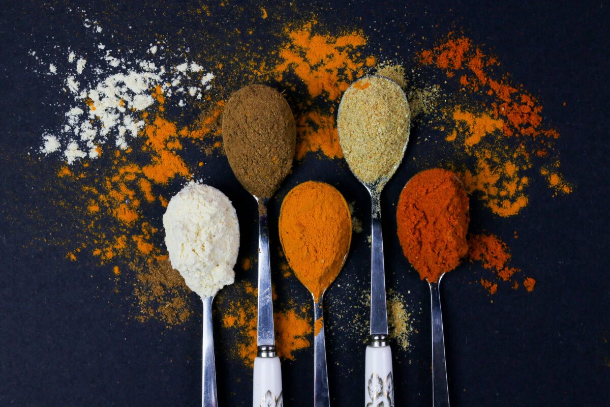 Five spoons full of various spices on a black background