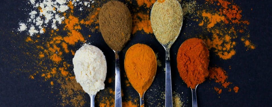 Five spoons full of various spices on a black background