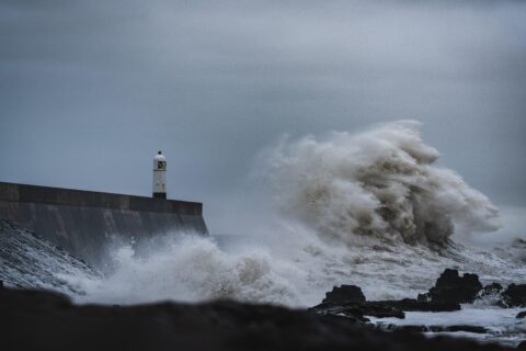 A stormy sea throws up a huge wave against a lighthouse standing firm