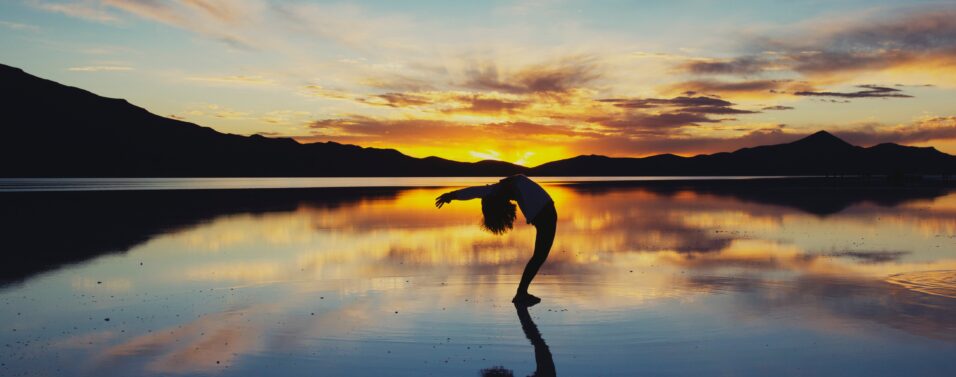 a flexible person bending on a beach at sunset