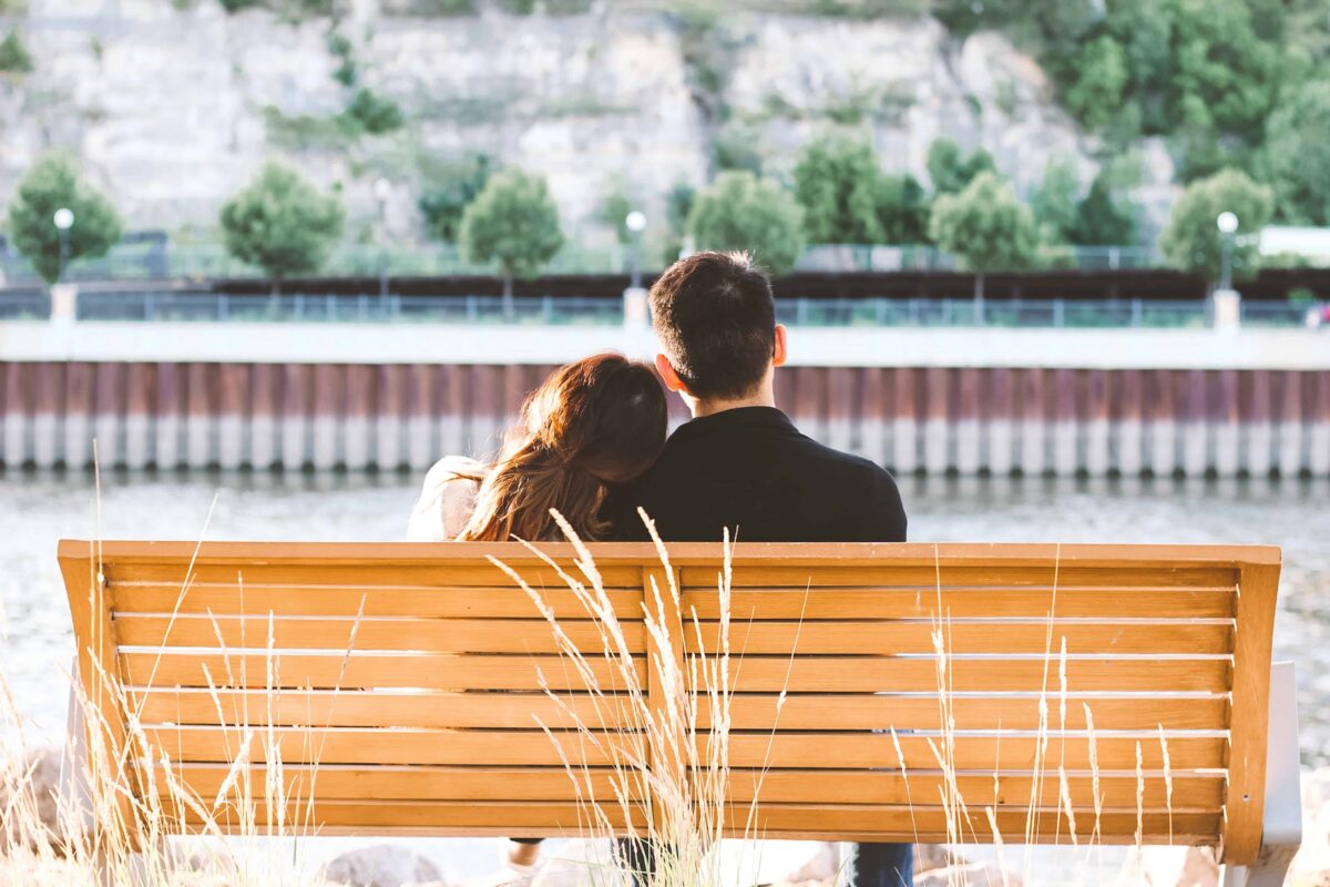 Copule sitting on a bench facing away with woman head resting on partners shoulder