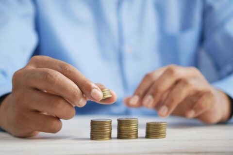 close up of a man stacking coins into three piles that are growing from left to right